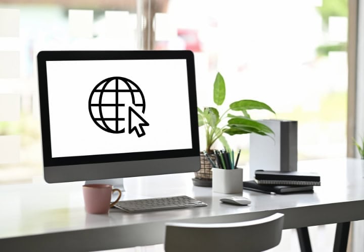 Computer on a white desk in a modern office with a graphic on the screen representing website design and development