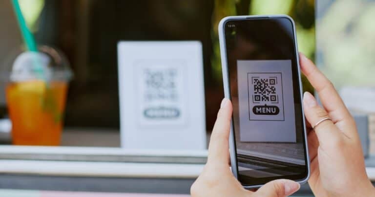 A person is holding a mobile phone and taking a picture of a QR code at a coffee shop that leads to a menu.