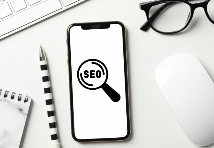 Modern white desk top with a phone that has an SEO search icon on the screen.